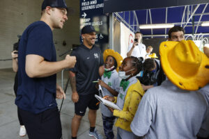 Children wearing costume hats look up and smile at two Yankee baseball players.