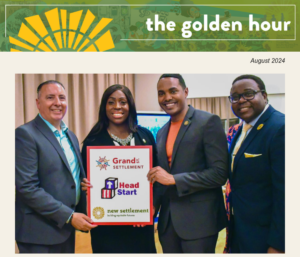 In this photo from "the golden hour" newsletter, August 2024 edition, four individuals are standing together holding a sign that features the logos of Grand Settlement and New Settlement, with "Head Start" prominently displayed in the center. The individuals are celebrating a partnership or achievement related to the Head Start program.